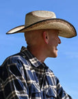 A man wearing a blue plaid polo and a brown straw cowboy hat