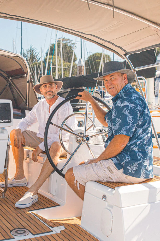 two men in a casual outfit sitting on a yacht wearing a brown and grey sun hat