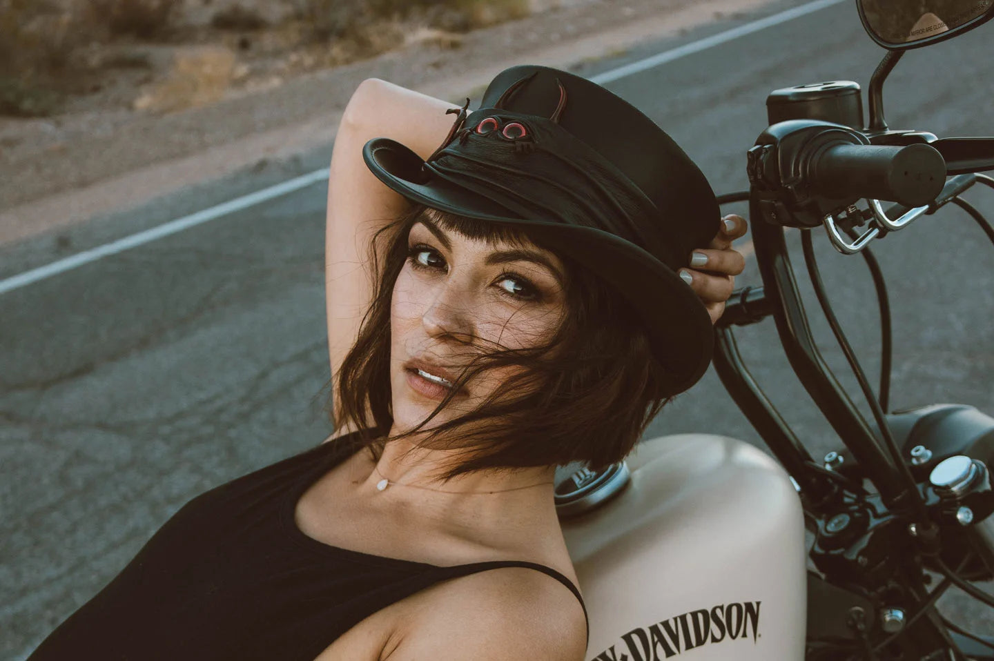 woman in black lying on her motorcycle wearing a black voodoo top hat by american hat makers