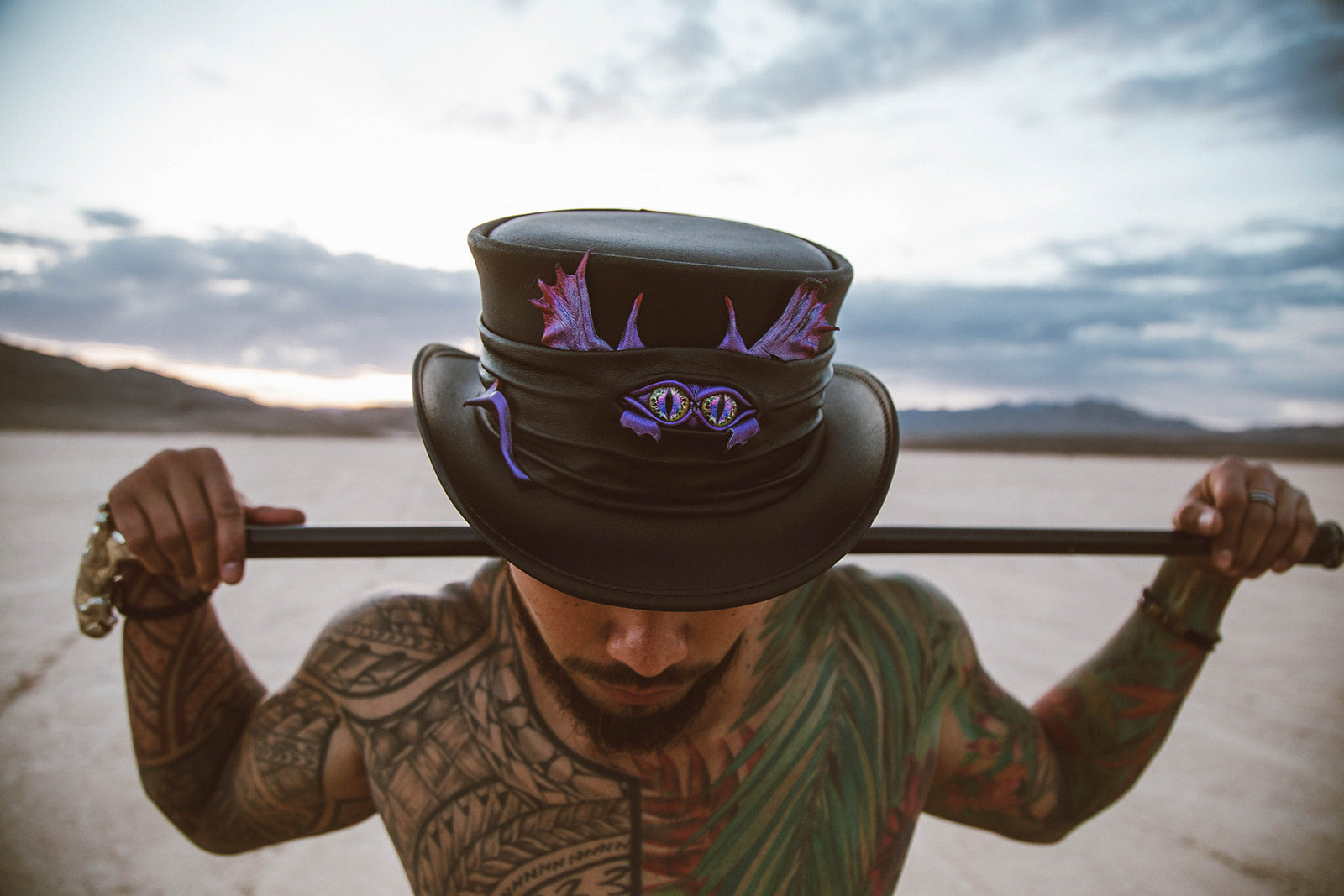 A man with a tattoo holding a cane and wearing a leather top hat