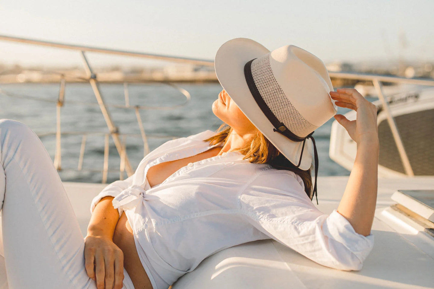 Woman lounging on boat wearing the milan cream womens sun hat by American Hat Makers