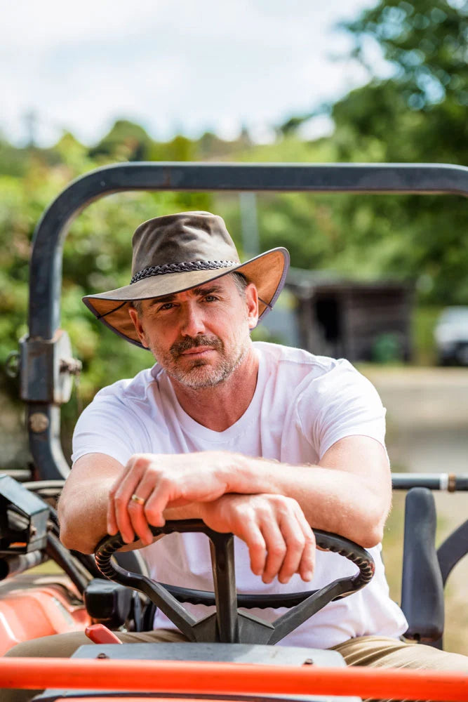 A man wearing a white shirt sitting on a tractor wearing a brown leather hat