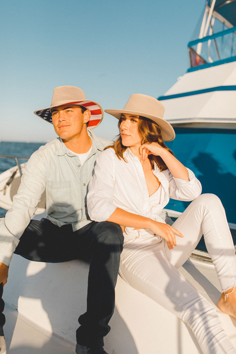 A man and a woman sitting on a boat wearing different kinds of sun hat