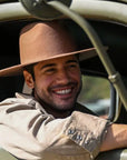 A man sitting inside a truck wearing a polo and a brown felt hat
