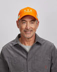 A smiling old man wearing an orange mesh cap and gray polo