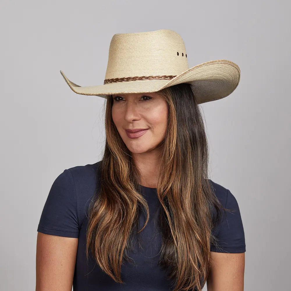 Woman smiling gently, wearing a straw cowboy hat with a braided band and a dark blue top