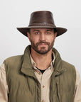 Man with a light stubble wearing a Chocolate Roughneck Outback Hat and an olive green jacket over a beige shirt