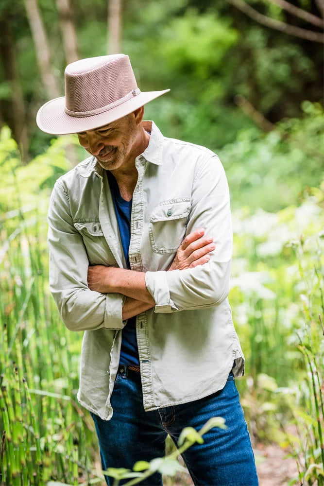 A man in a garden wearing a cream colored jacket and a brown mesh hat
