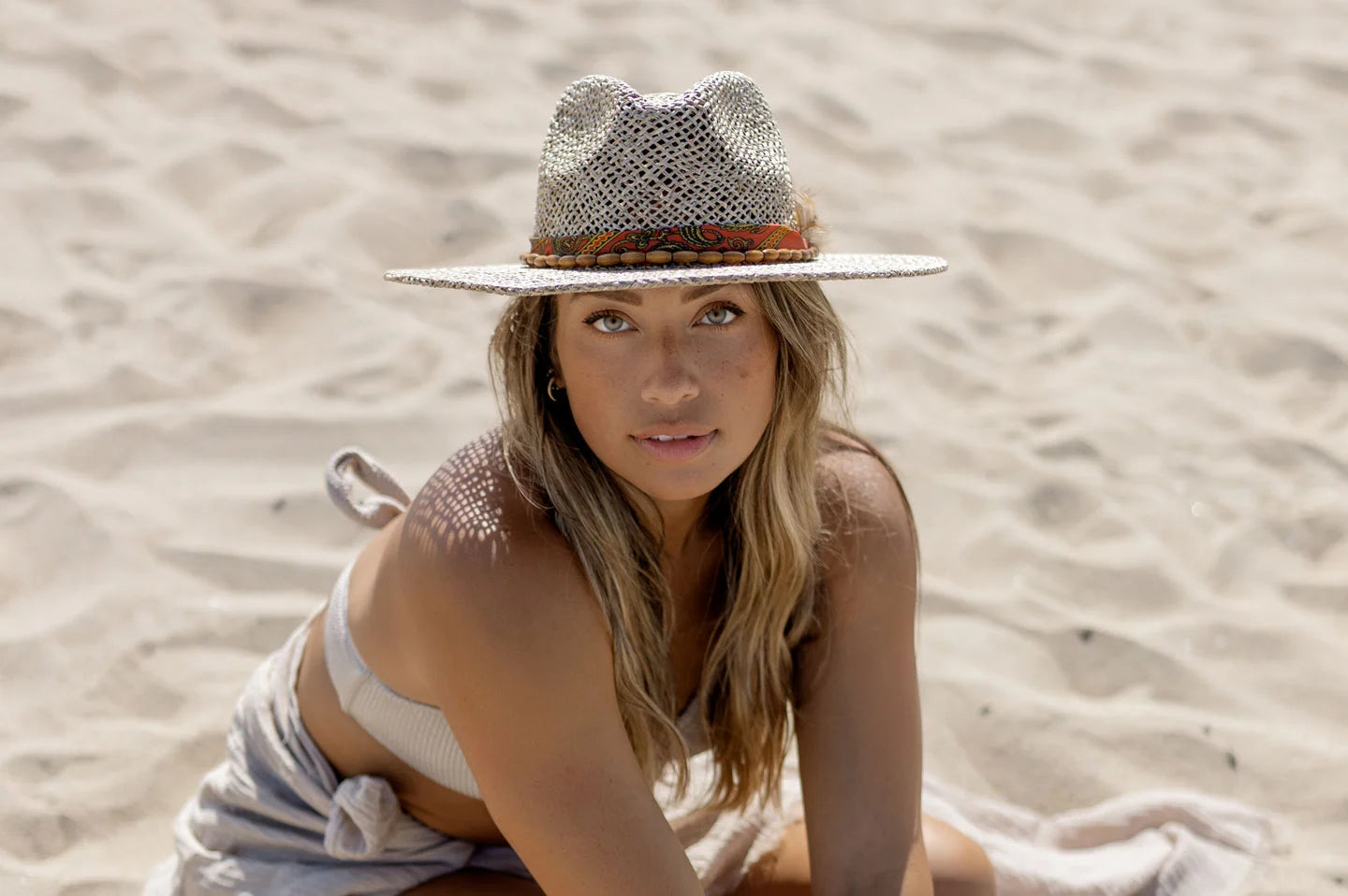 Woman sitting at beach while wearing the Savannah straw sun hat by American Hat Makers