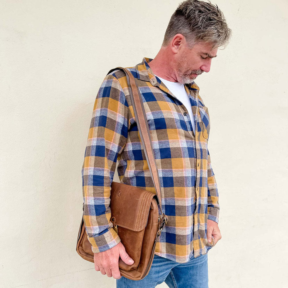 A man wearing a plaid shirt and jeans with a brown leather bag