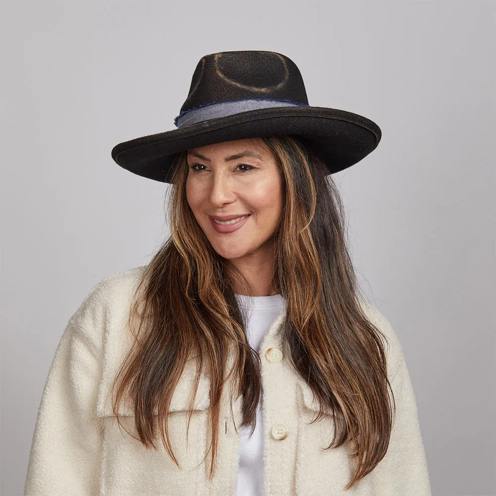 Woman with long brown hair smiling and wearing a Small Town felt fedora hat and white buttoned-up coat.