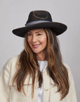 Woman with long brown hair smiling and wearing a Small Town felt fedora hat and white buttoned-up coat.