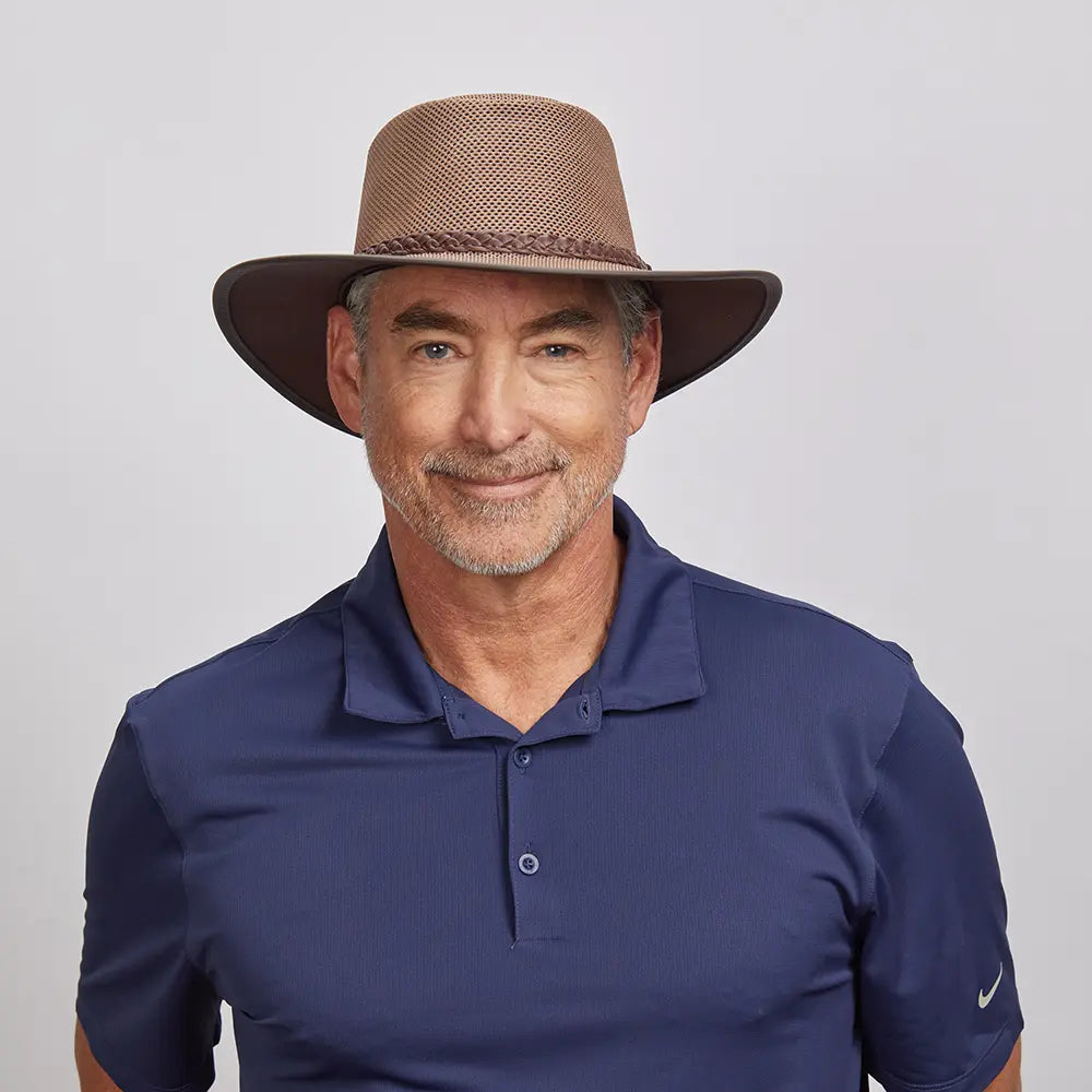 Middle-aged man with a friendly smile, wearing a brown mesh hat and a dark blue polo shirt