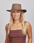 Smiling woman with blonde hair wearing a brown mesh hat and brown sleeveless top