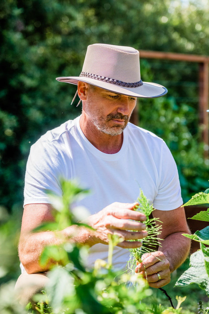 A man holding plants wearing an eggshell sun hat 