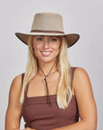 Smiling woman with blonde hair wearing a beige mesh hat and brown sleeveless top