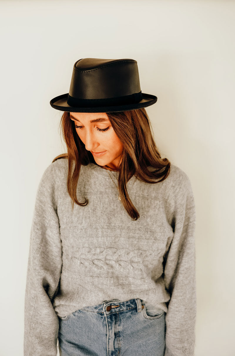 A woman in a sweatshirt wearing soho black leather hat