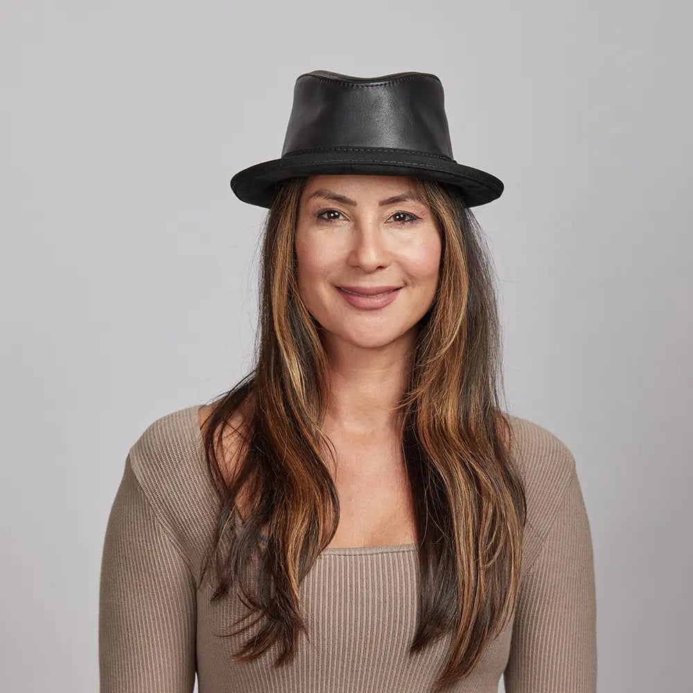 Woman with long brown hair wearing a black leather hat and a beige top, smiling