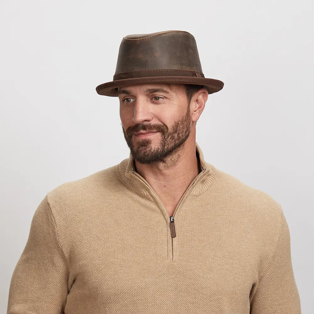 Man with a light stubble wearing a Soho Fedora Hat and beige zip-up sweater, looking slightly to his left with a soft smile.