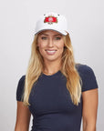 A blonde woman smiling, wearing a white Stay Humble cap and a navy blue top.