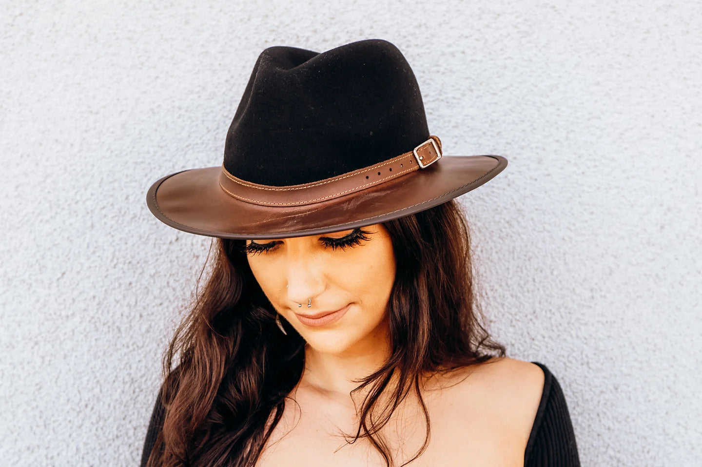 woman in black leaning on a wall wearing a black hat by american hat makers