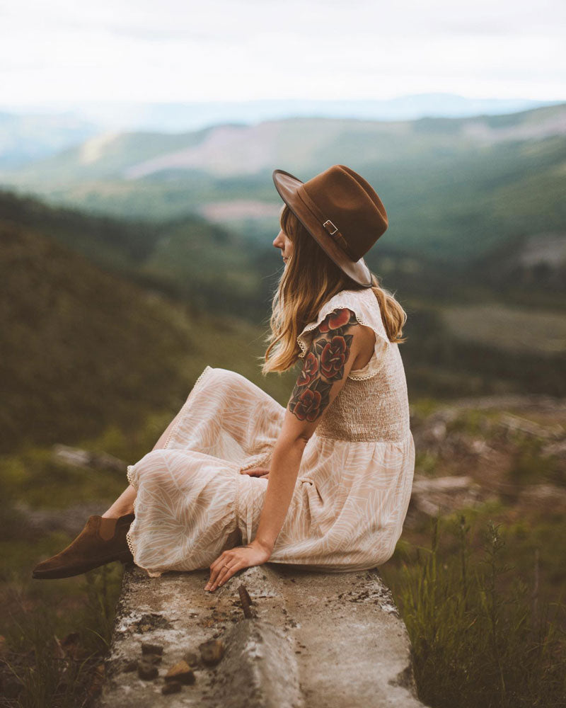 A woman sitting outdoors with mountain view wearing felt leather fedora hat