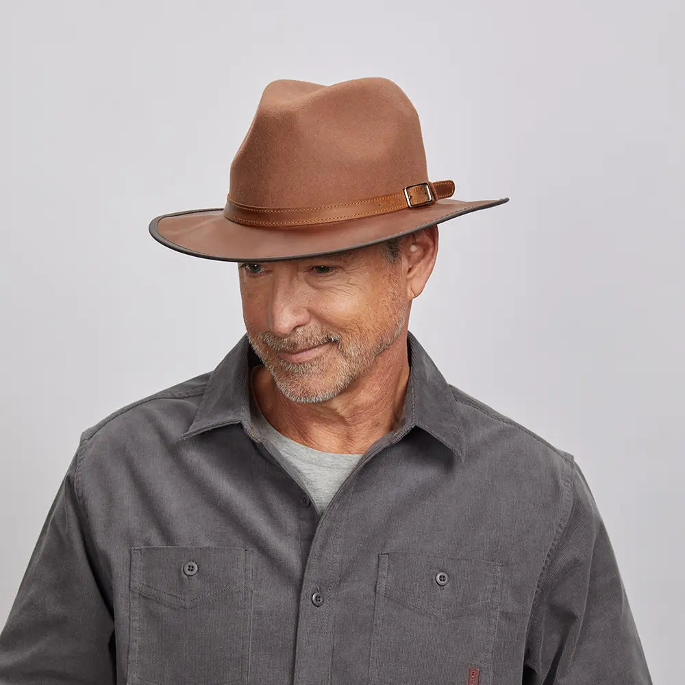 A man with a light stubble wearing a felt saddle fedora hat and a gray button-up shirt.