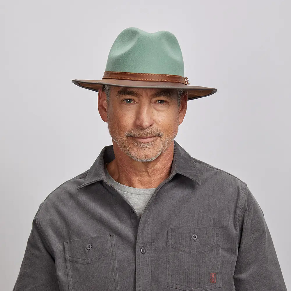 A man with a light stubble wearing a felt sage fedora hat and a gray button-up shirt.