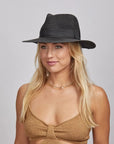 A blonde woman wearing a Black Afternoon Fedora Hat and a brown knitted top.