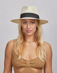 A blonde woman wearing a Cream Afternoon Fedora Hat and a brown knitted top.