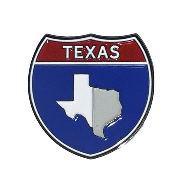 A shield-shaped Texas emblem pin or badge with a red top section, white 'TEXAS' text, and a blue lower section containing a white and silver outline of Texas, shown on a plain white background.