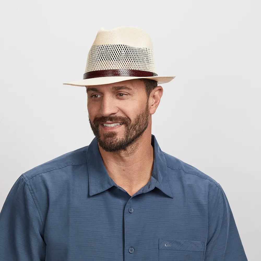 A smiling man in a navy blue polo wearing a cream straw fedora