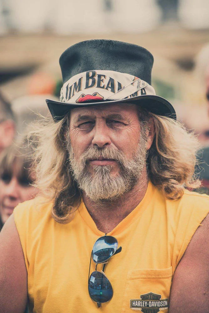 A man wearing a yellow sleeveless shirt wearing a black top hat