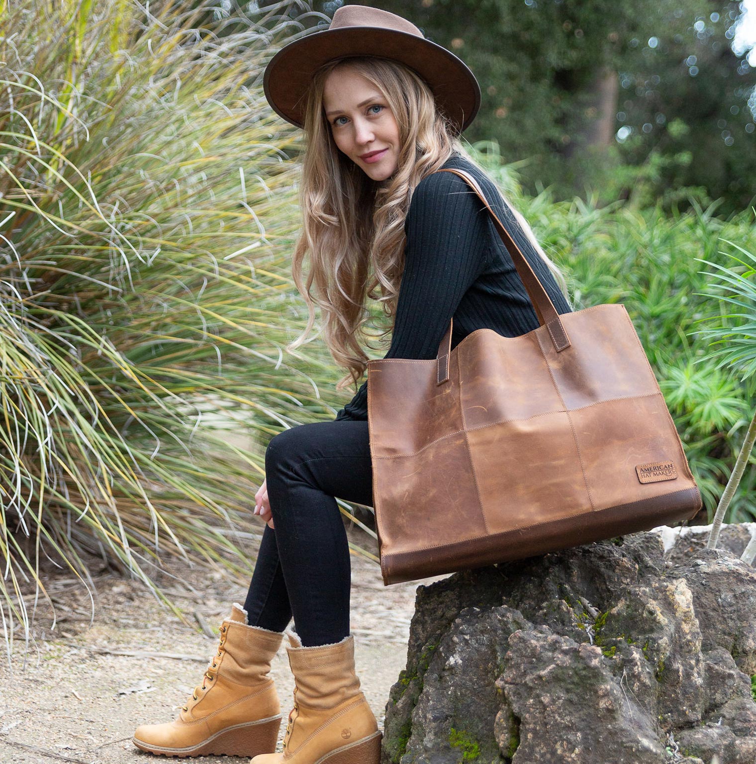 woman sitting on a rock with a large brown american hat maker tote