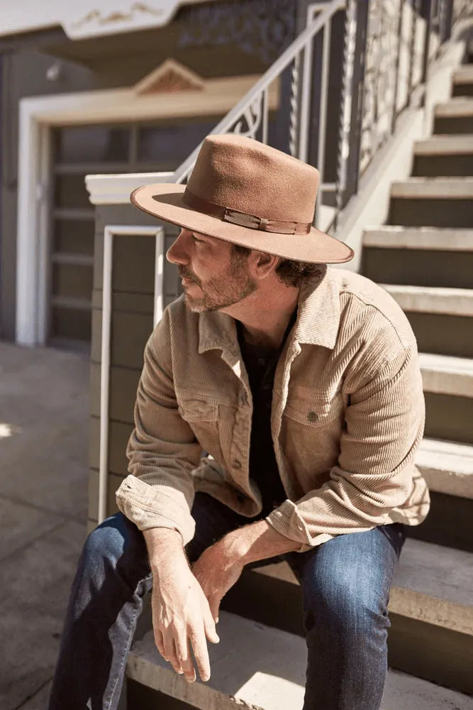 A man sitting on the stairs wearing a brown jacket and felt hat