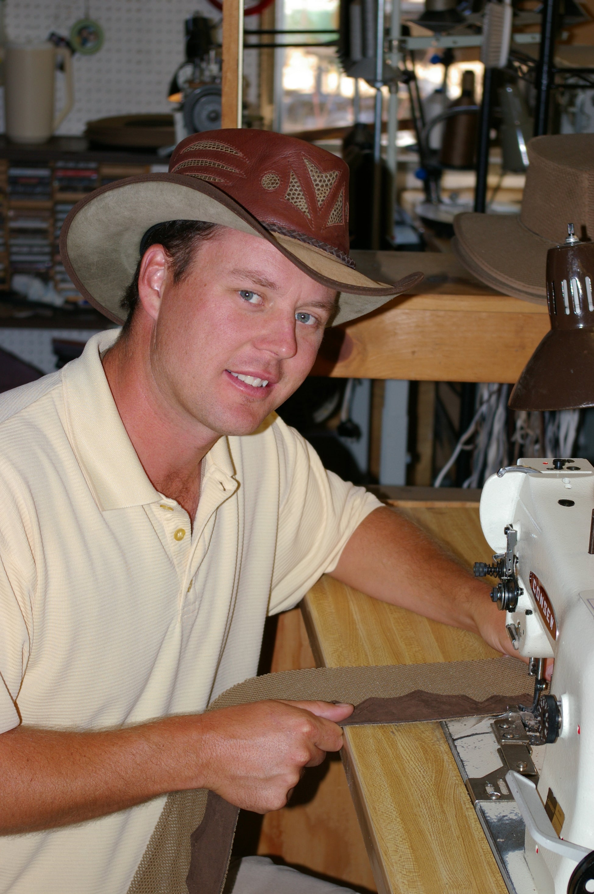 A man wearing a cream polo and a brown hat sewing leather material
