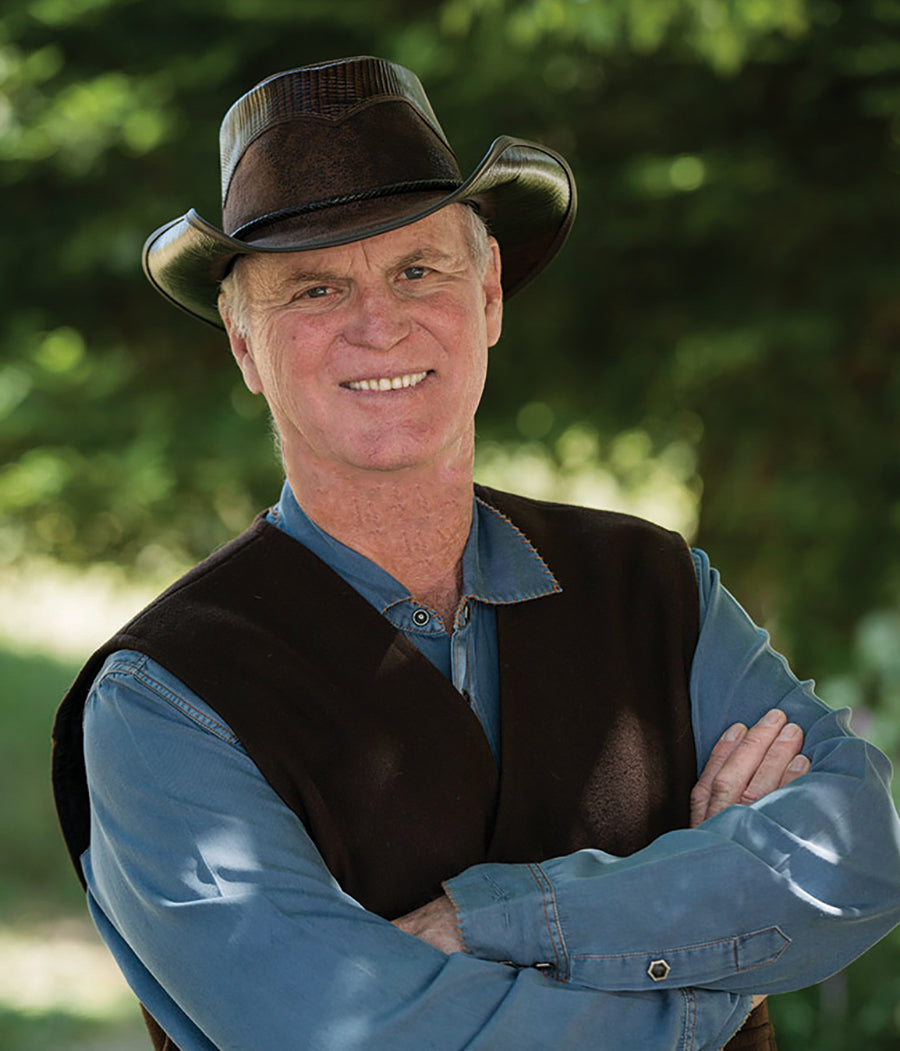 A man standing outdoor wearing a blue polo jacket with dark top and a cowboy hat