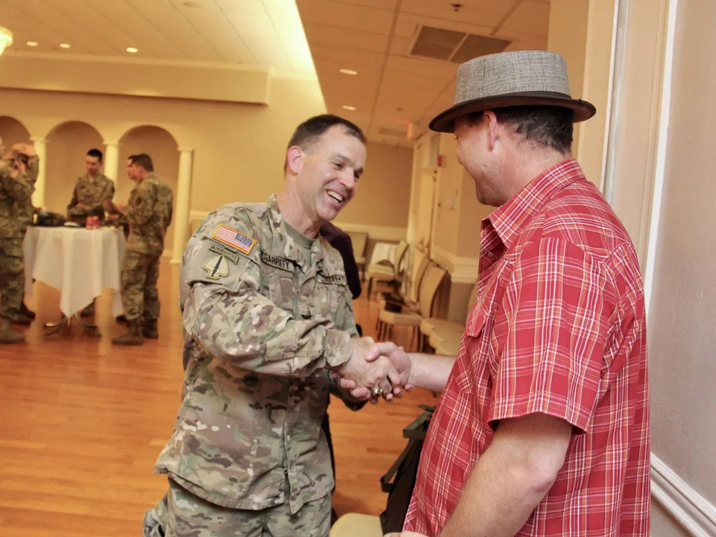 An American soldier shaking hands with a man wearing a brown fedora