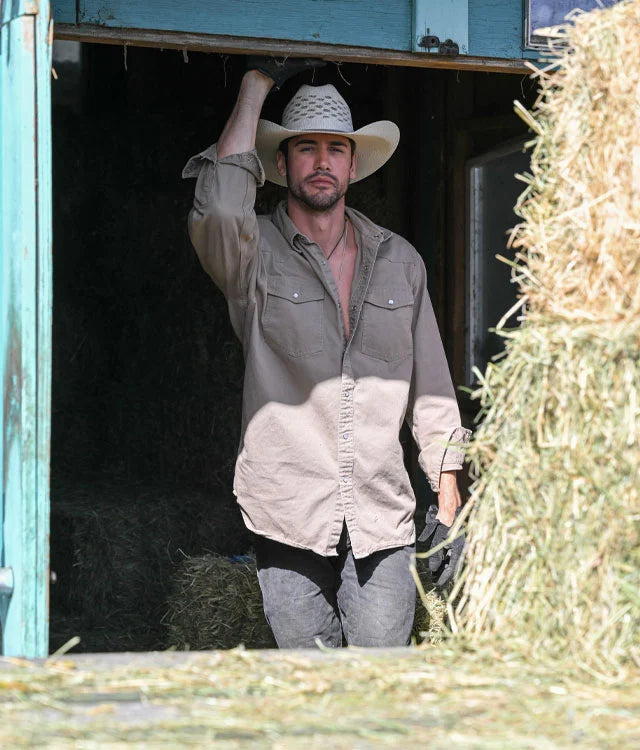 A man standing in between a pile of hay with his cowboy hat