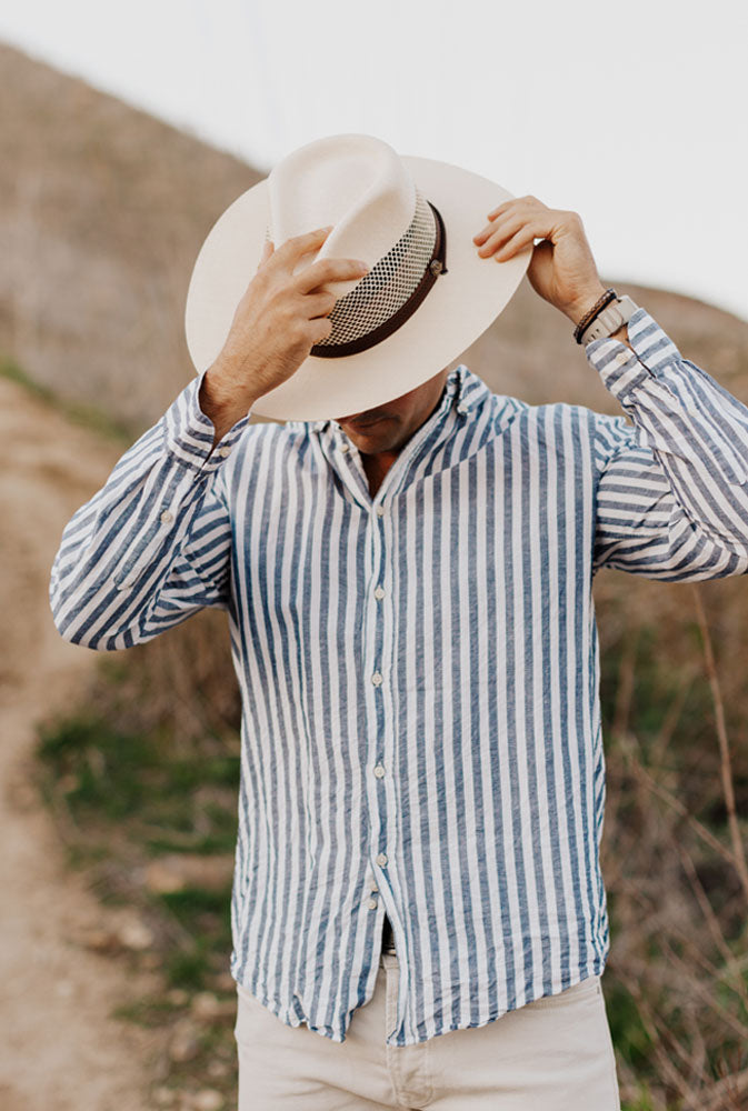 A man in his stripe polo and khaki jeans fixing his cream straw hat