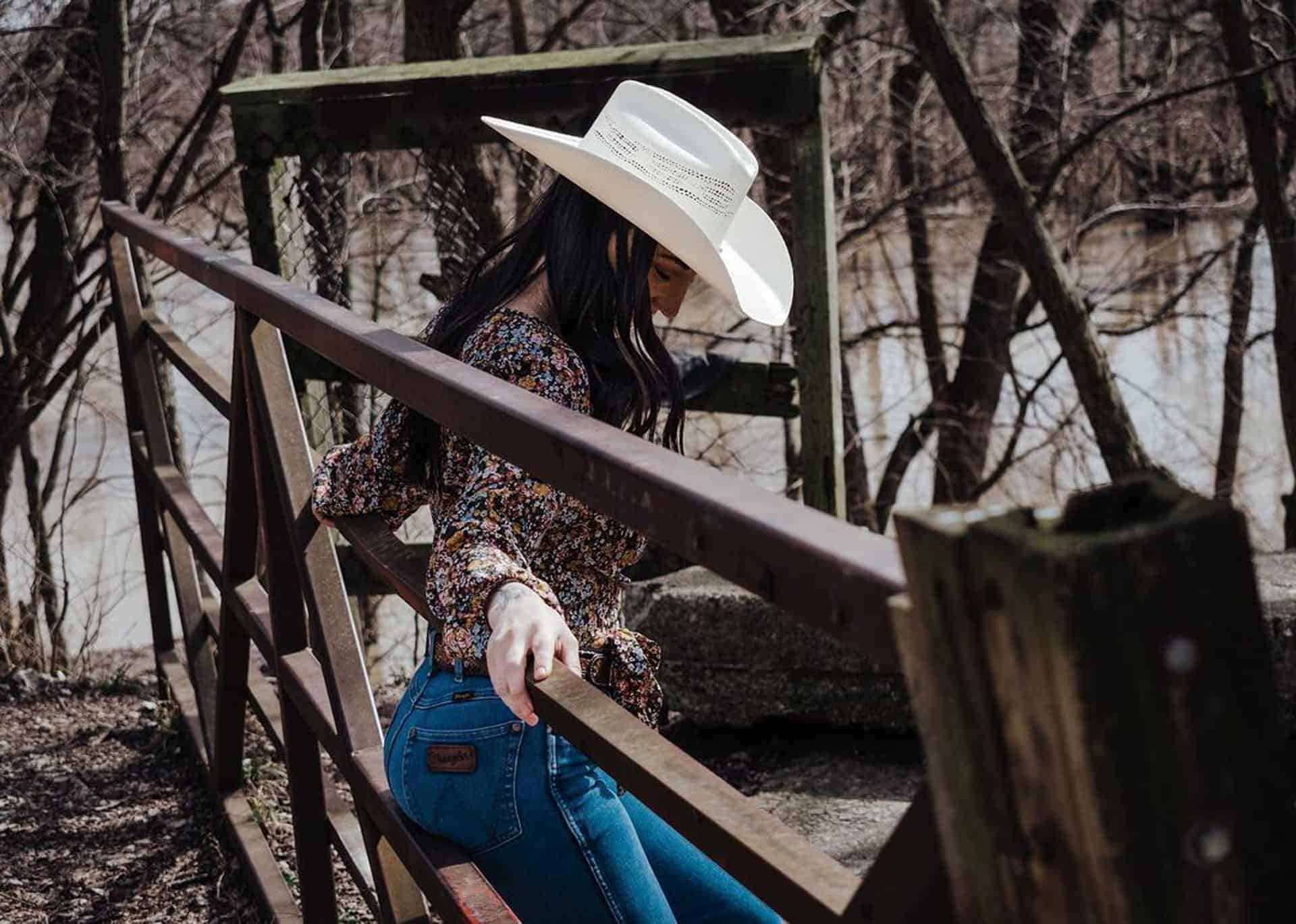 A woman leaning on a railing wearing a white cowboy hat