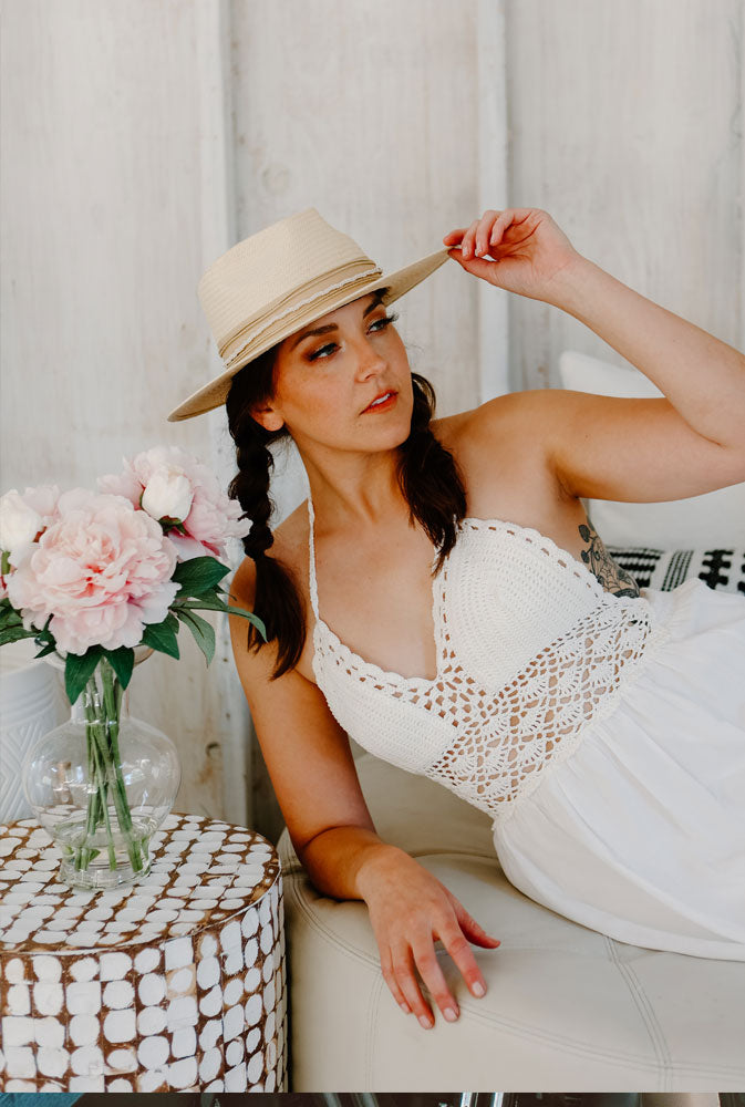 A woman wearing a white dress lying on a couch holding her cream straw hat