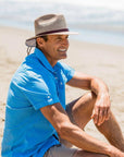 Man sitting on beach wearing the tan Milan mens sun hat by American Hat Makers