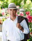 Man standing near flowers wearing the cream Milan mens straw hat with Leather hat band