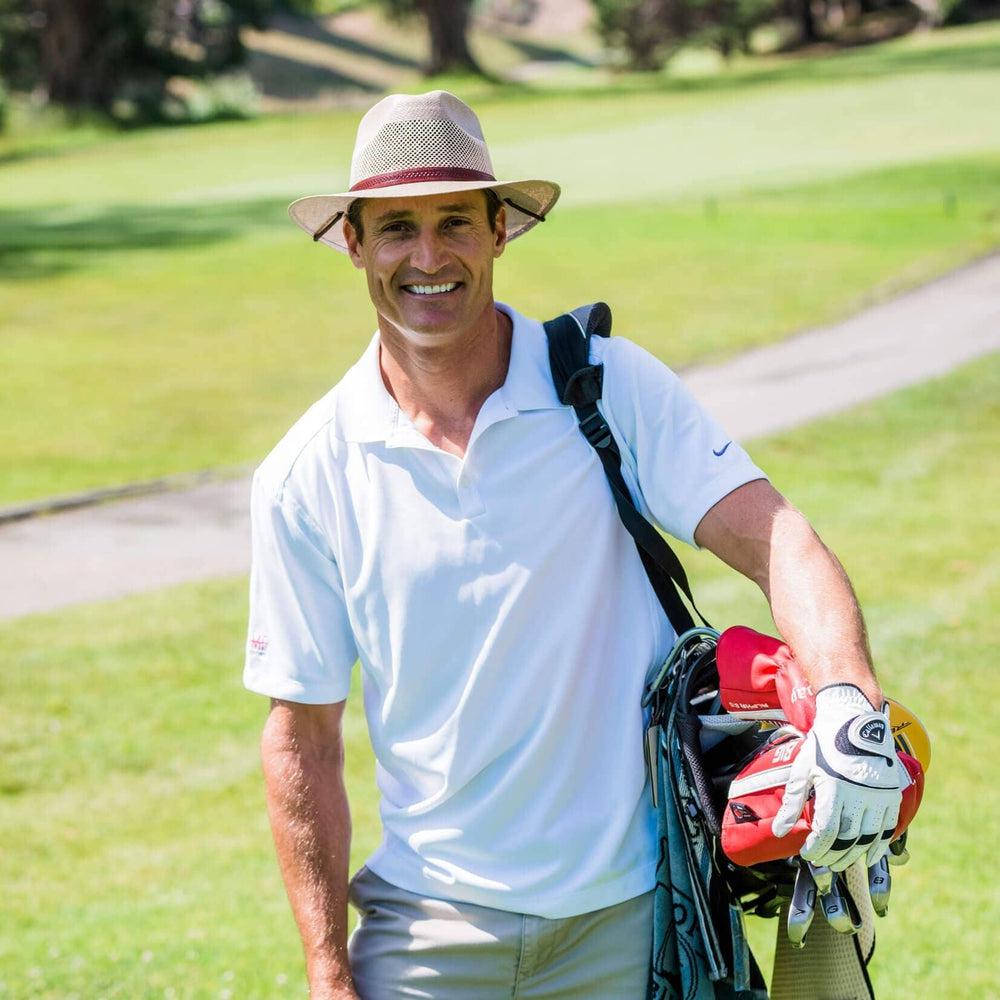 Man holding golfing club bag while wearing the mens Milan Tan straw sun hat with leather hat band