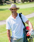 Man holding golfing club bag while wearing the mens Milan Tan straw sun hat with leather hat band