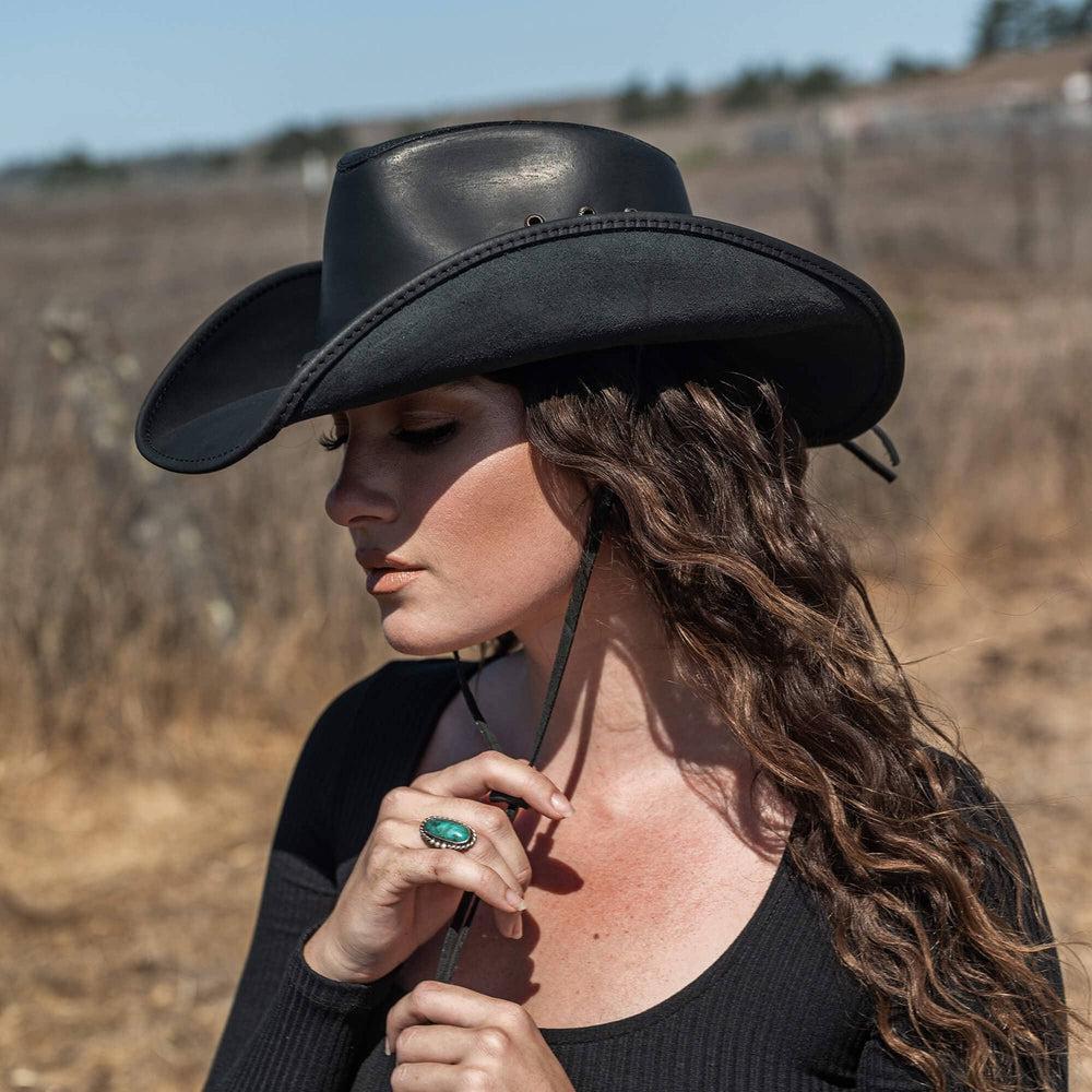 A woman standing outdoors wearing black leather cowboy hat