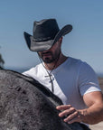 A man wearing a leather cowboy hat touching a horse