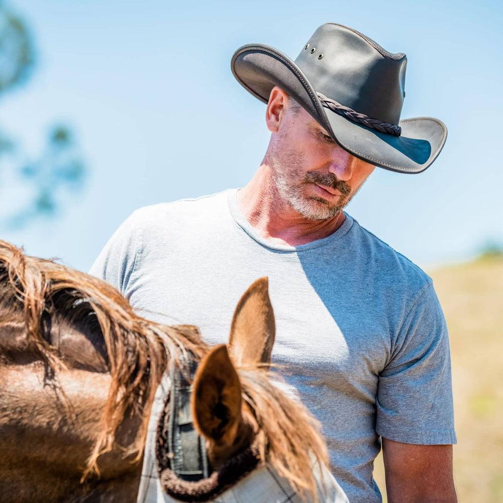 A man wearing Hollywood Black Leather Cowboy Hat taking care of the horse