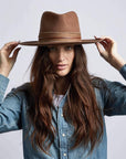 A woman in denim jacket wearing Jawa Brown Wide Brim Felt Fedora hat holding it with two hands